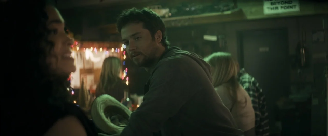 Holiday Harmony (2022) movie still: medium — A dimly lit bar interior features patrons sitting at a counter with ambient decorations. A man in a…