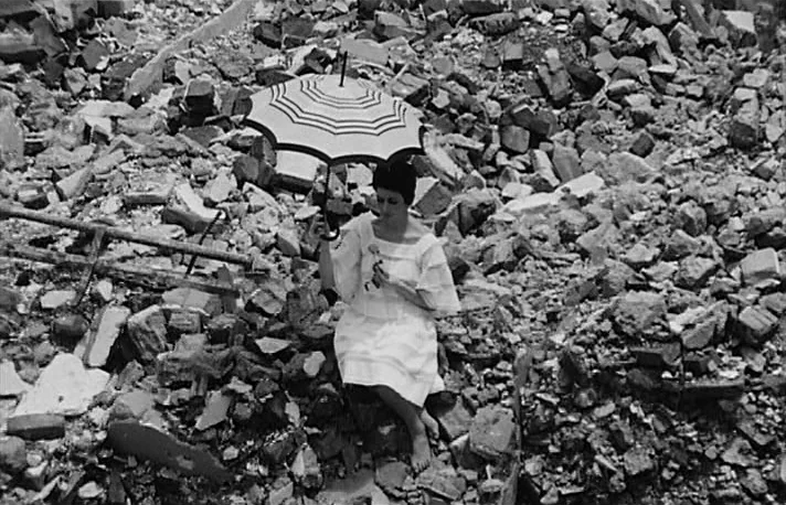 Fando y Lis (1968) movie still: fullbody — A woman sits on top of a massive mound of broken concrete and bricks. She holds a small decorative…