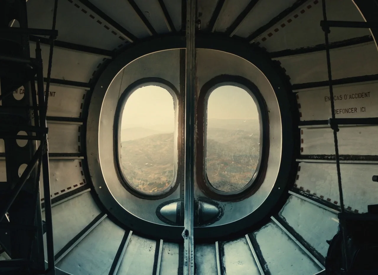 Red Island (2023) movie still: establishing — The interior of an aged aircraft fuselage shows rounded windows overlooking a distant landscape.…