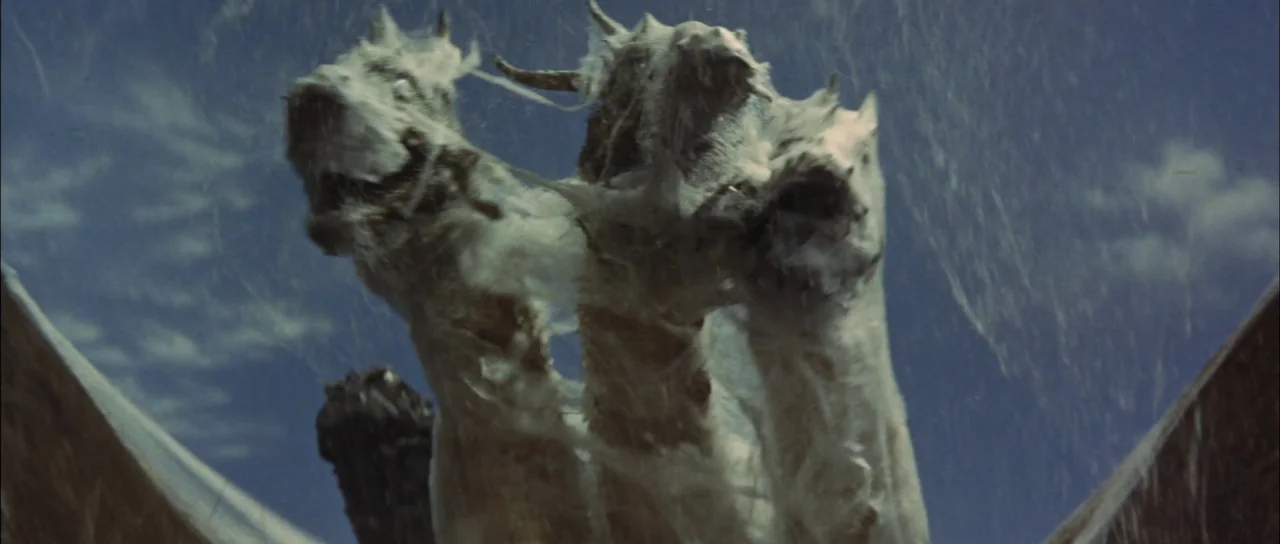 Ghidorah The Three Headed Monster (1964) movie still: closeup — A three-headed dragon figure emerges against a bright blue sky filled with wispy…