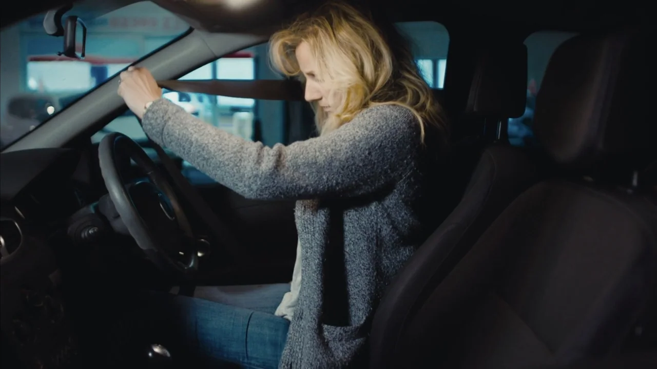 You Might Get Lost (2021) movie still: medium — A modern car interior with dark upholstery and visible dashboard controls. A blonde woman pulls her…