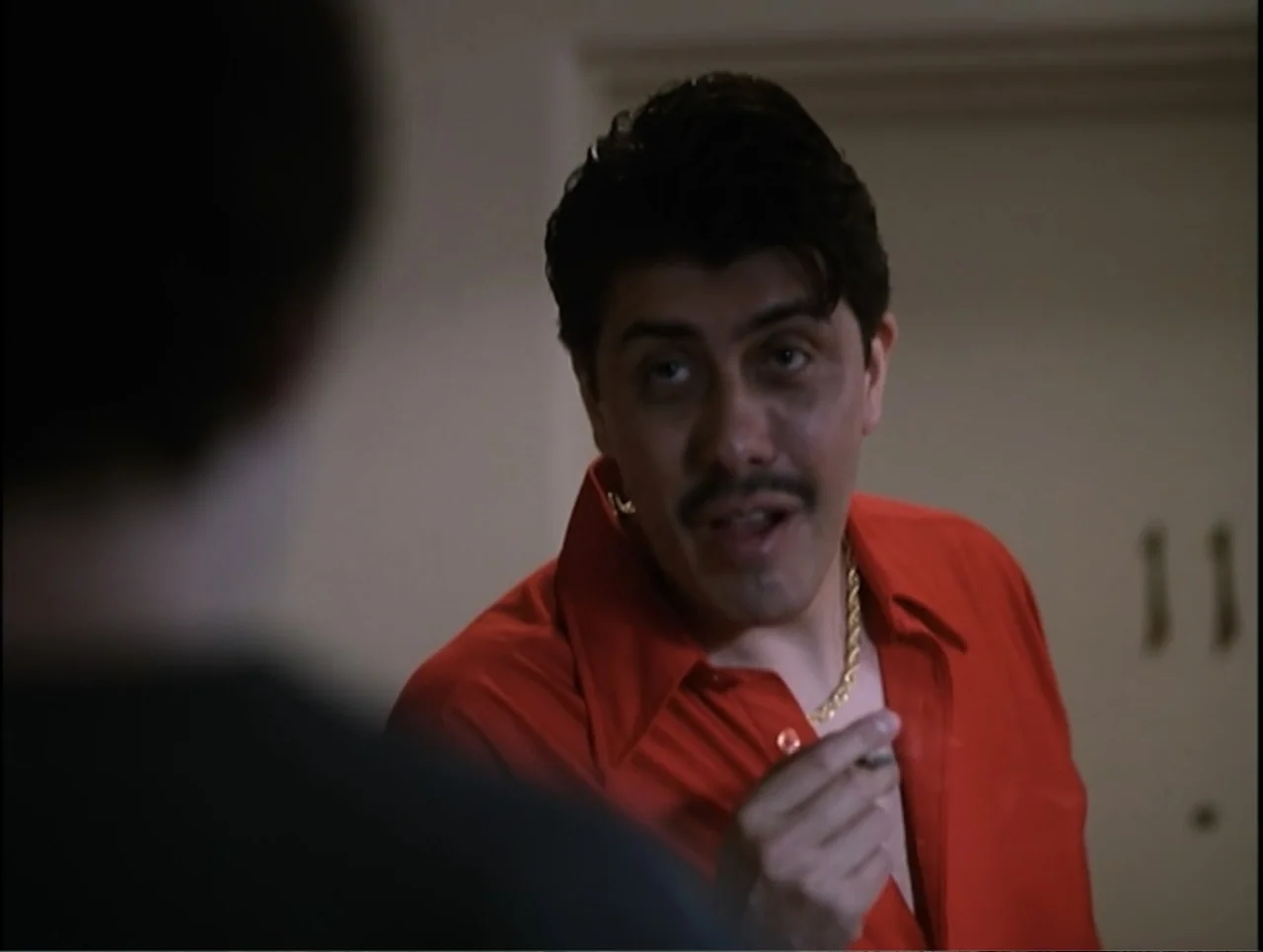 Apartment 12 (2001) movie still: medium — An interior motel room wall with a numbered door is visible in the background. A man in a red shirt…