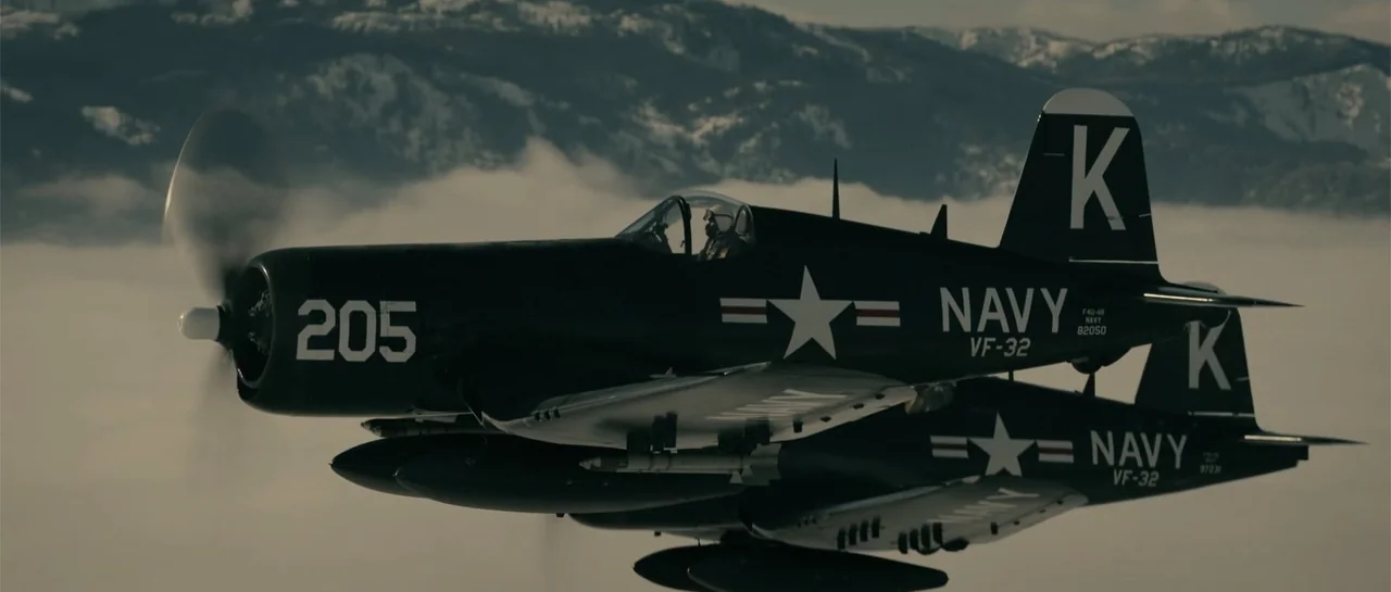 Battle of the Bulge (1965) movie still: medium — Two F4U Corsair fighter planes fly in formation above a thick bank of clouds. The navy aircraft are…