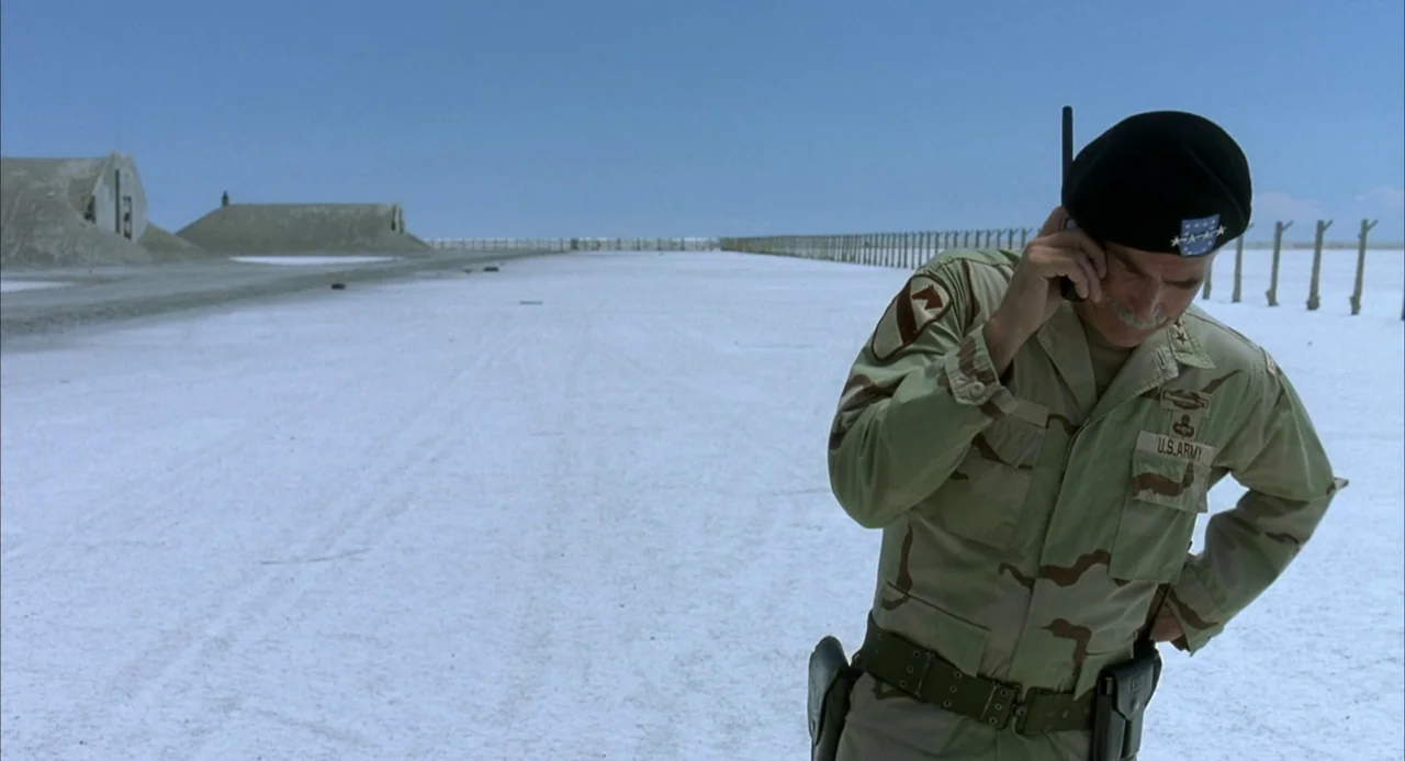 Hulk (2003) movie still: medium — A vast, flat white salt plain stretches toward a distant fenced boundary under clear skies. A high-ranking army…