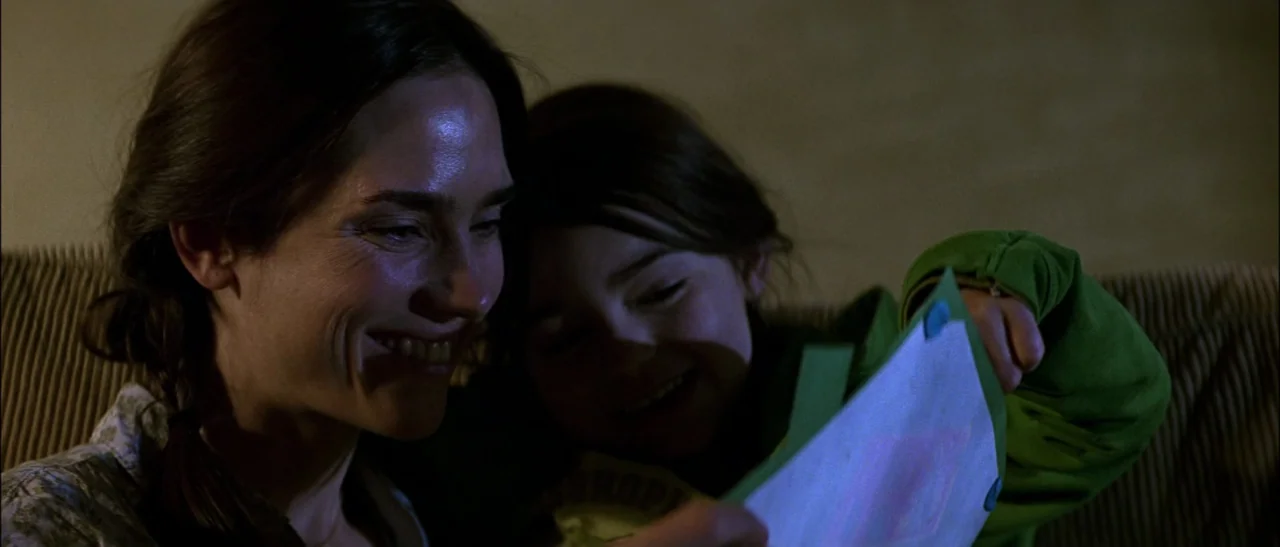 Dark Water (2005) movie still: medium — A dimly lit indoor space with the subjects seated on furniture. A woman and young girl look at a drawing in…