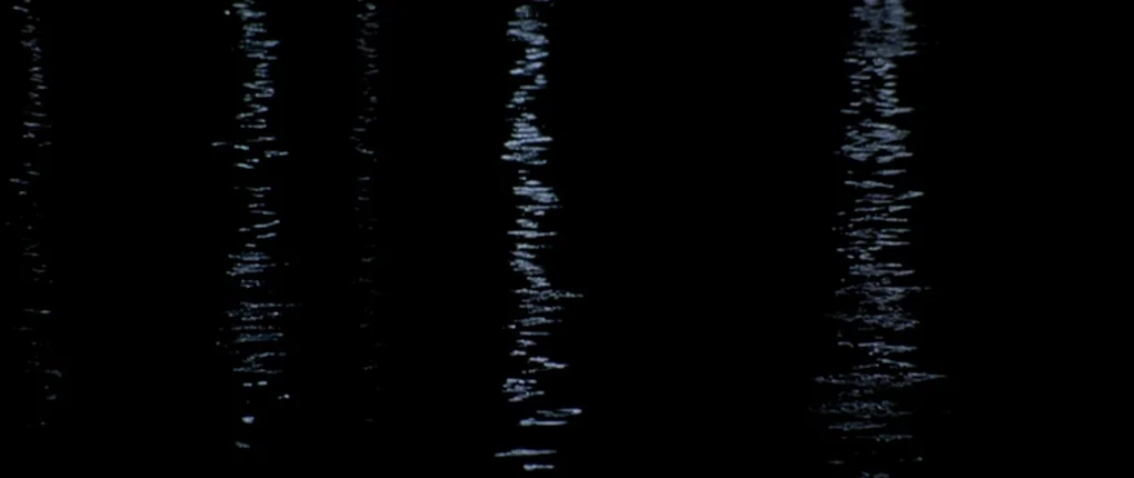 The Usual Suspects movie still: establishing — Dark water surface with vertical light reflections created by ripples. The scene consists entirely of…