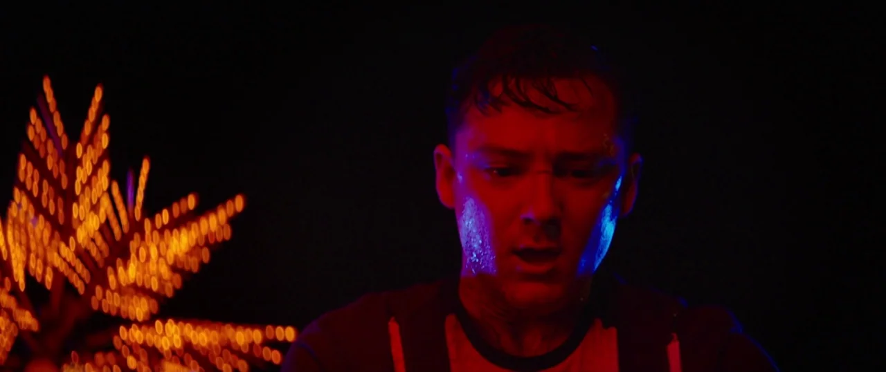 The Strangers: Prey at Night (2018) movie still: closeup — A dark outdoor space at night with bright blurred orange lights in the background. A…