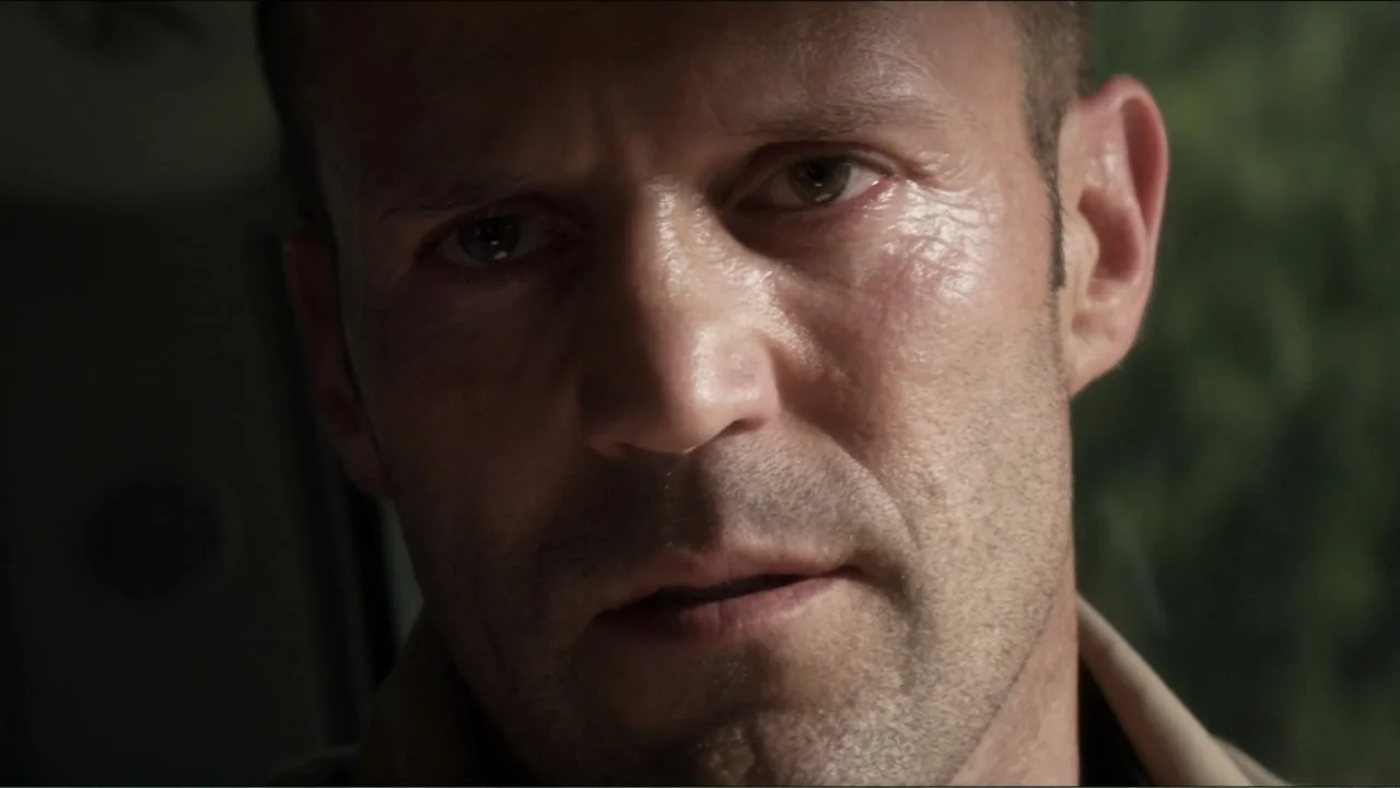 Parker (2013) movie still: closeup — A close shot inside a car with a blurry green exterior visible. A man looks ahead through the windshield.