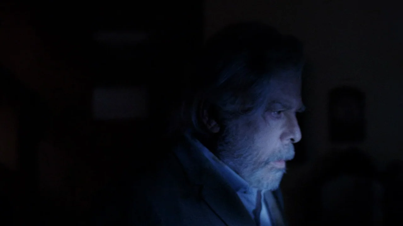 The Sect (1991) movie still: closeup — A dark space features a man lit by the cold glow of a screen. The man faces the right side of the frame while…
