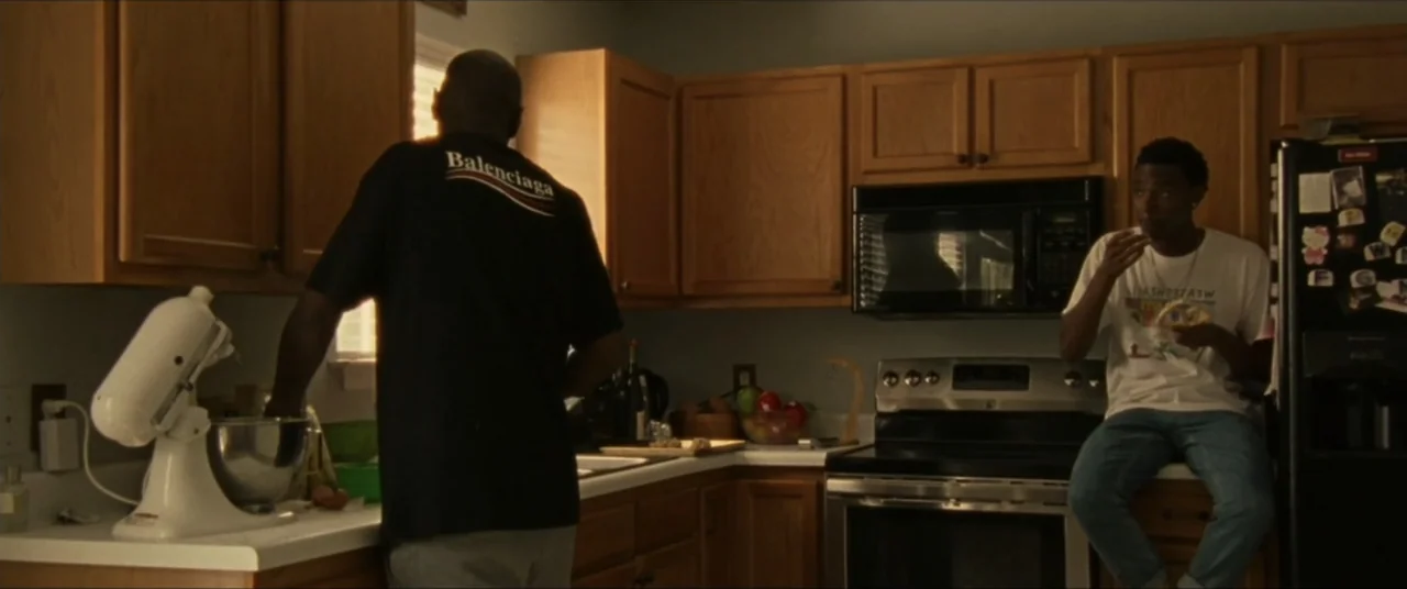 Sermon on the Mount (2019) movie still: medium — A residential kitchen features wooden cabinetry, a stainless steel stove, and a white countertop.…