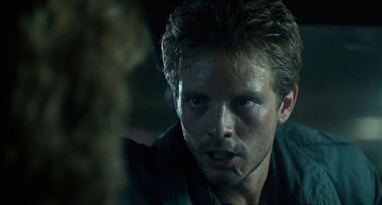 The Terminator (1984) movie still: closeup — A dark vehicle cabin provides the setting for a high-tension interaction at night. A man with a scar on…