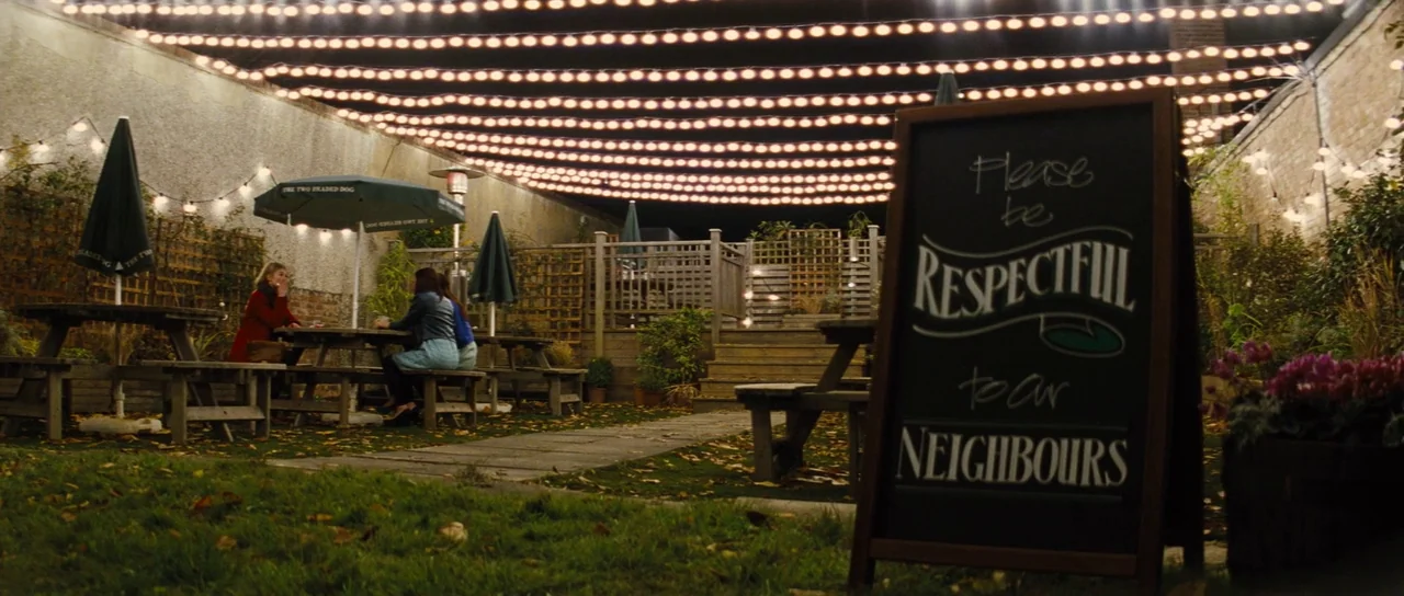 The World’s End (2013) movie still: wide — A nighttime outdoor pub area featuring wooden picnic tables and strings of glowing lights. A large…