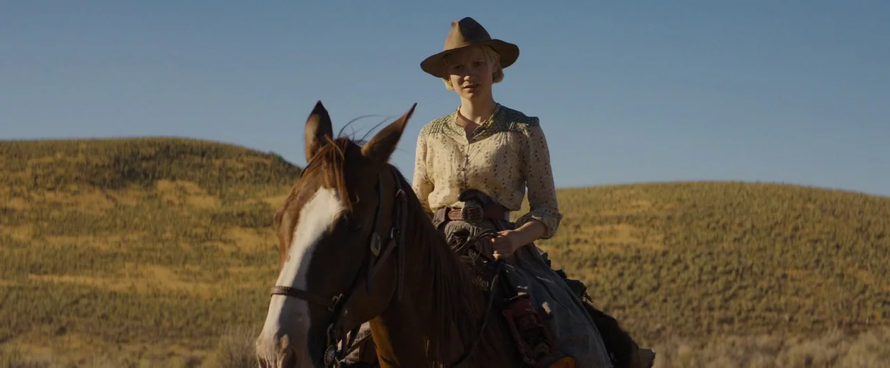 Damsel (2018) movie still: medium — A woman rides a horse across a vast, rolling prairie landscape under blue skies. She wears a period-accurate…