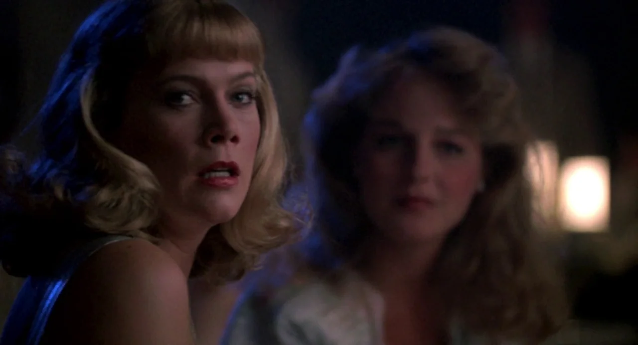 Peggy Sue Got Married (1986) movie still: medium — Two women are seated in a dark, dim interior space with soft background lighting. The primary…