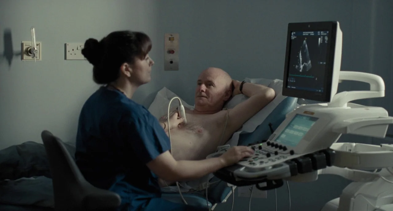 I, Daniel Blake (2016) movie still: medium — A medical examination room features light blue walls and a digital ultrasound machine. A technician in…