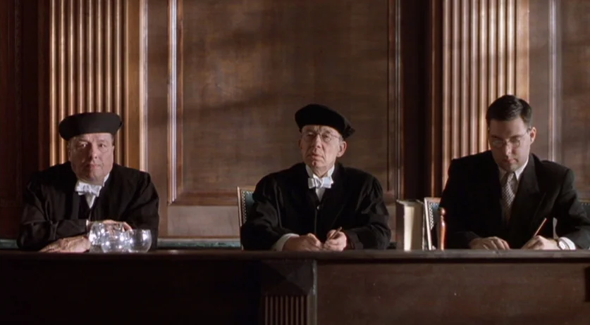 Invincible (2001) movie still: medium — A dark, wood-paneled room features a long bench occupied by three seated men. The subjects are arranged…