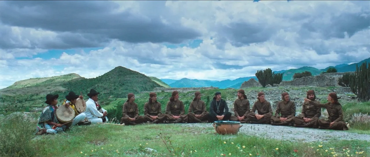 The Holy Mountain (1973) movie still: wide — A group of people dressed in similar brown tunics sit in a wide circle. They are gathered in a grassy…