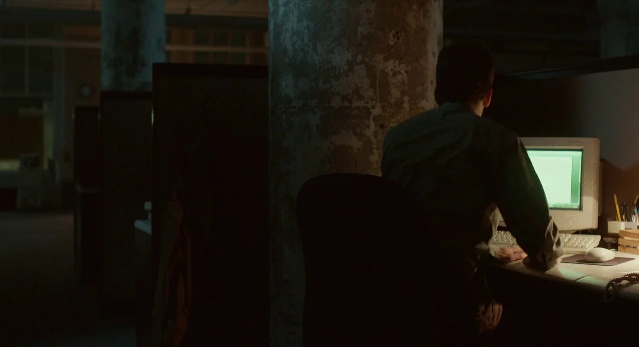 The Art of Self Defence (2019) movie still: medium — An empty, dimly lit workspace features rows of cubicles and large weathered concrete columns. A…