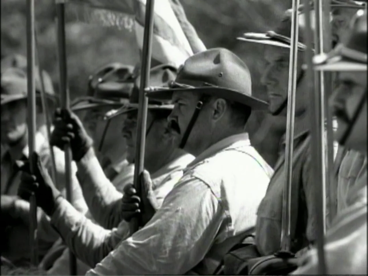 In Pursuit of Honor (1995) movie still: medium — A group of men stand in a line outdoors holding long wooden poles. The men wear mid-nineteenth…