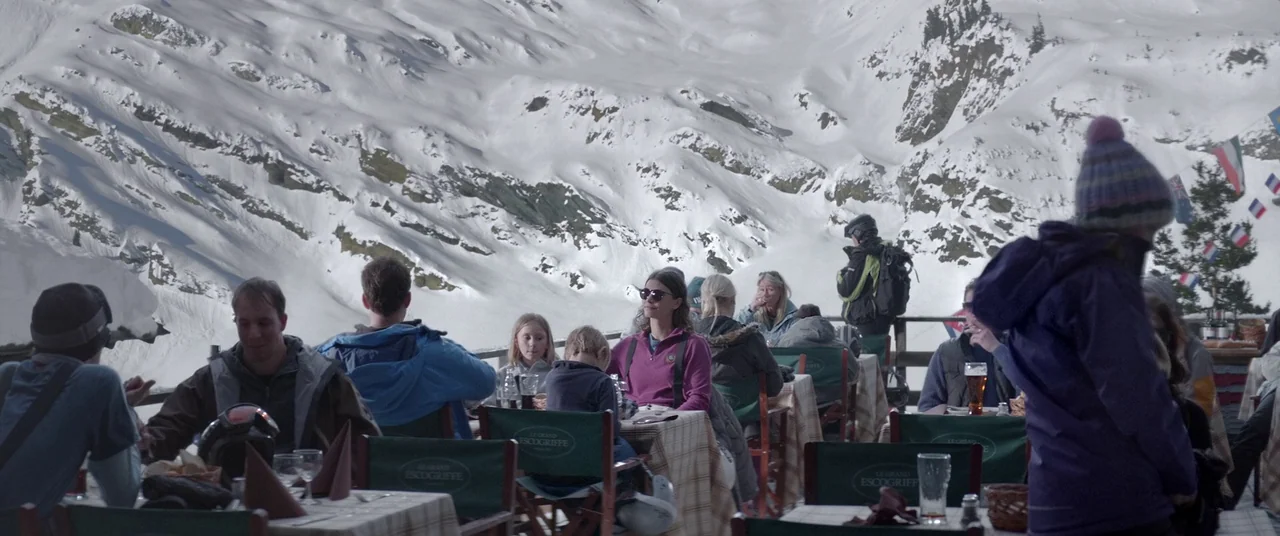 Force Majeure (2014) movie still: wide — A crowded outdoor restaurant terrace is positioned at the base of a snowy mountain. Several groups of…