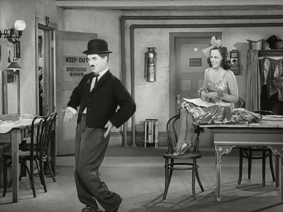 Modern Times (1936) movie still: fullbody — A well-lit dressing room features doors labeled 'Keep Out' and 'Please Knock'. A man in a suit performs…