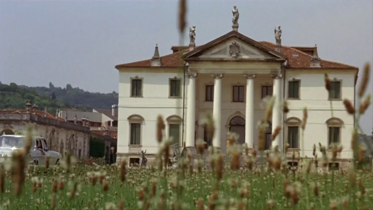 A Quiet Place In The Country (1968) movie still: establishing — A classical white villa with tall columns sits behind a field of wildflowers. A…