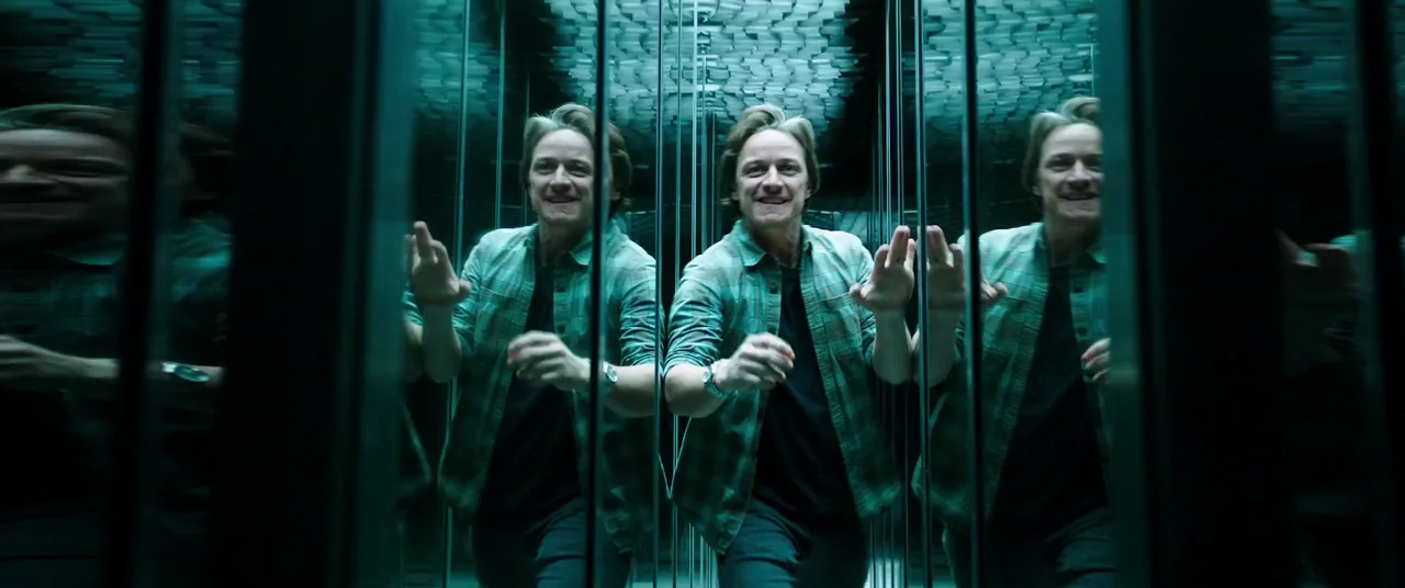 It Chapter Two (2019) movie still: medium — A man stands within a narrow corridor of reflective glass walls and mirrored panels. He walks forward…