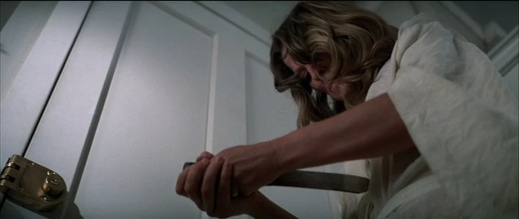 Demon Seed (1977) movie still: medium — A stark white interior wall features a closed door with a prominent brass lock. A woman in a white robe…