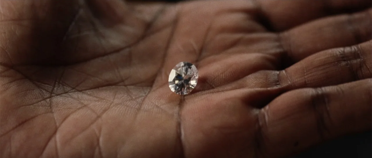Inside Man (2006) movie still: closeup — A close view shows a human palm with a loose, clear diamond sitting centrally. The skin texture is visible…