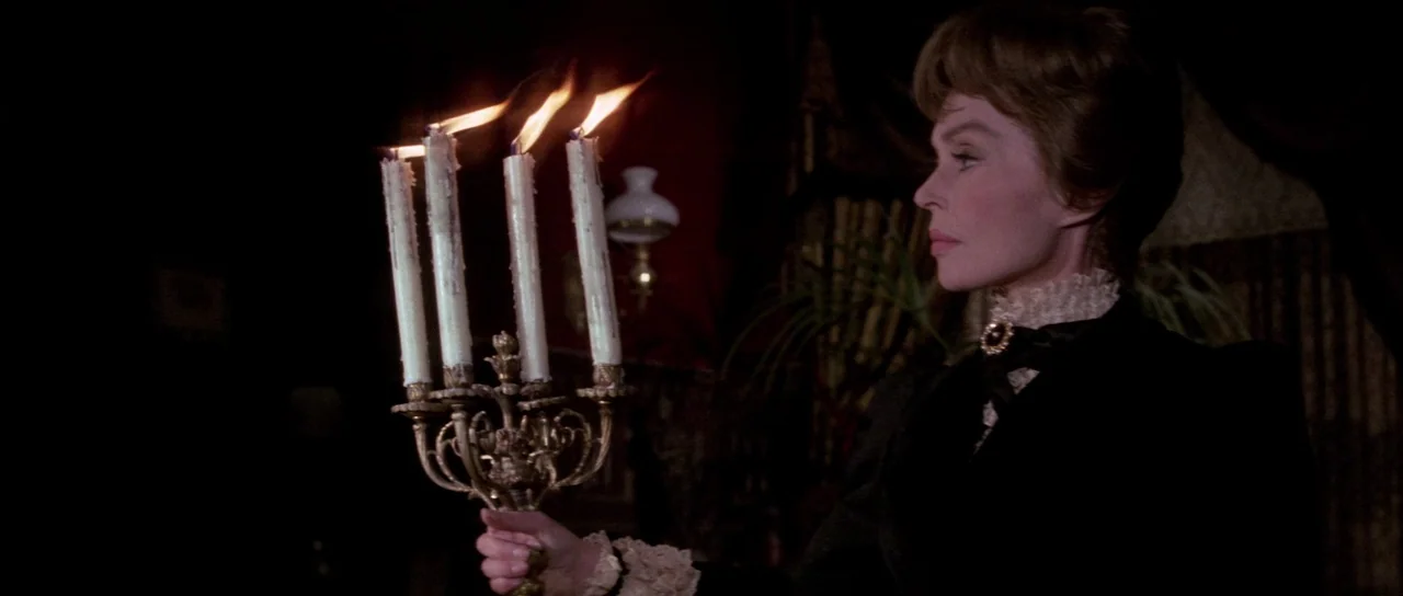 The House That Screamed (1969) movie still: medium — A dimly lit room with dark walls features a woman in Victorian-era clothing. She holds a brass…