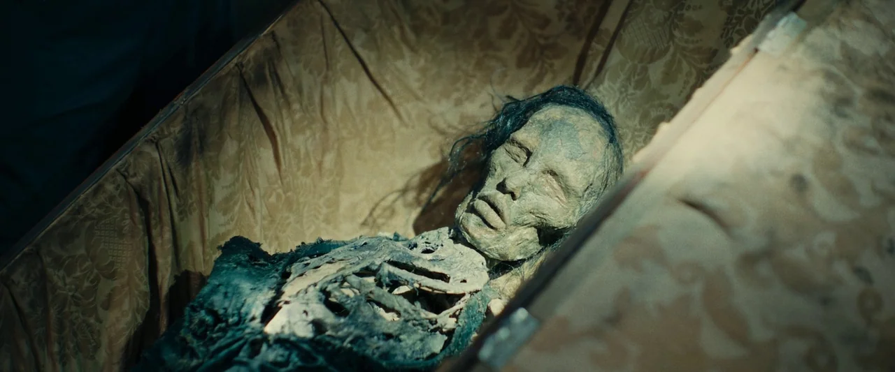 We Are Zombies (2023) movie still: closeup — A skeletal figure rests within a silk-lined coffin with patterned fabric walls. The corpse is…
