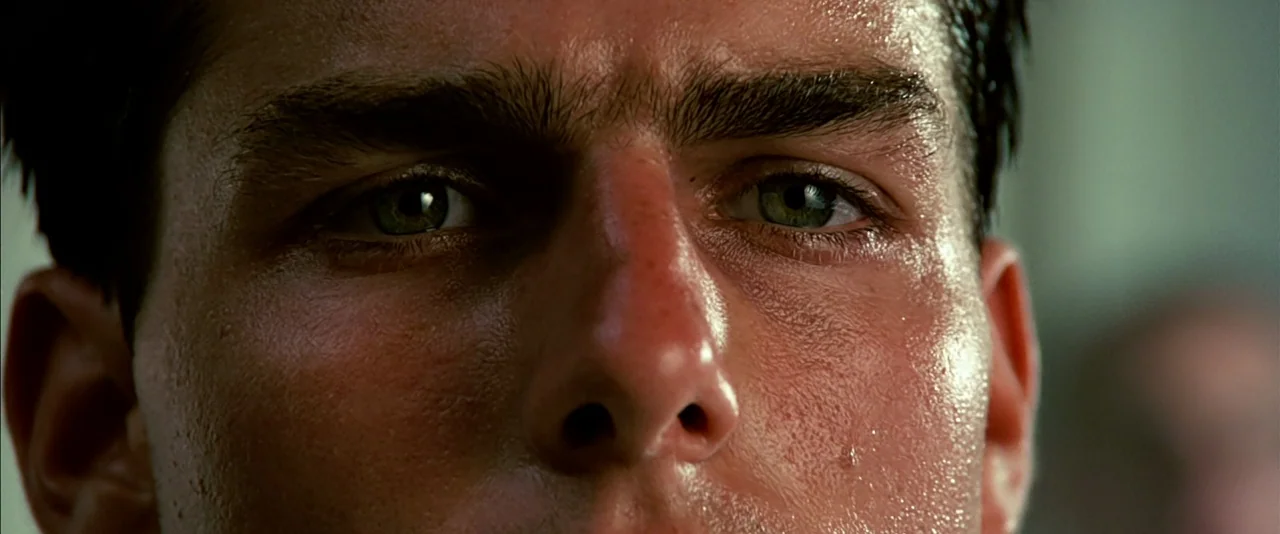Top Gun (1986) movie still: closeup — A close-up view focuses on a man's face against a blurred industrial background. The subject maintains a…