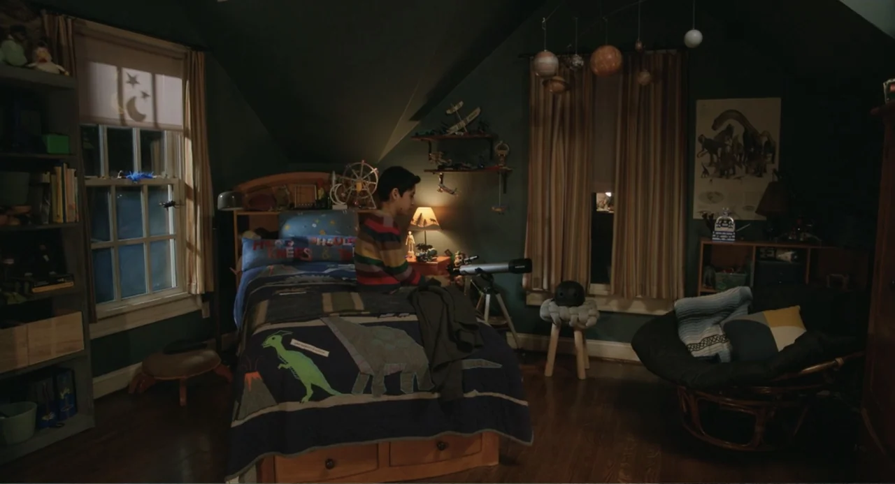 Harold and the Purple Crayon (2024) movie still: wide — A dimly lit child bedroom with dark green walls, dinosaur-themed bedding, and a model solar…