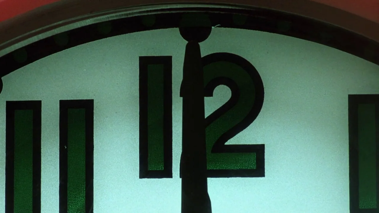 The Thin Blue Line (1988) movie still: closeup — A close-up of a clock face displays the number twelve in large black font. The clock hands are…