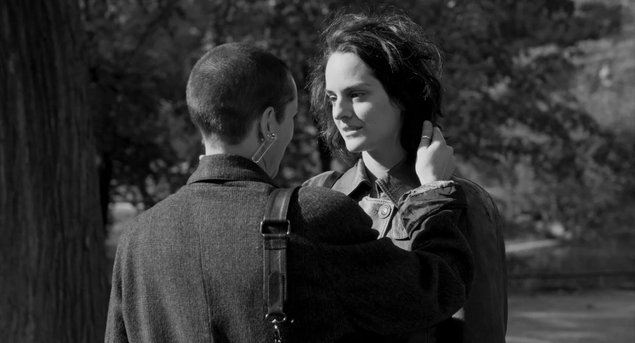 Paris, 13th District (2021) movie still: medium — A park setting with a large tree trunk on the left side. Two women stand close together while one…