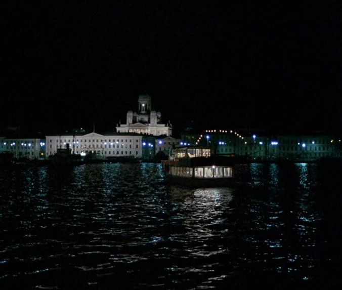 Crime & Punishment (1983) movie still: establishing — A dark harbor at night shows a small illuminated ferry on the water. In the background, a…