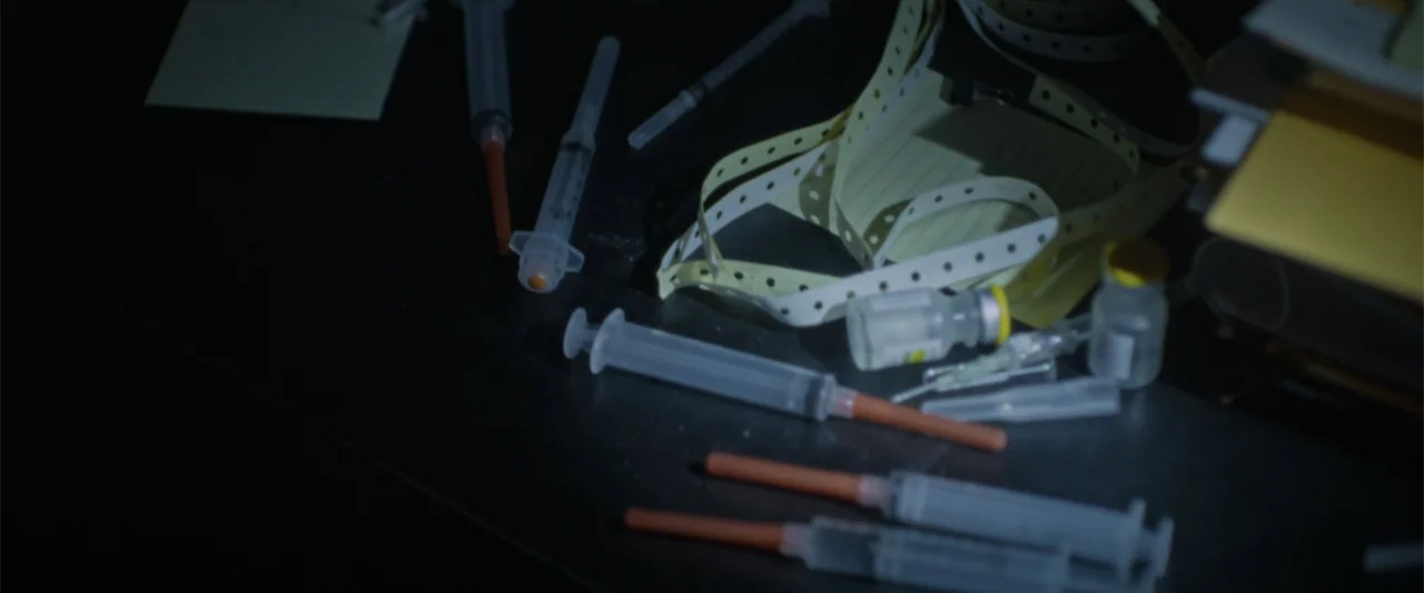 Silent Night, Deadly Night (2025) movie still: closeup — A dark table surface holds several scattered medical syringes and small glass medicine…