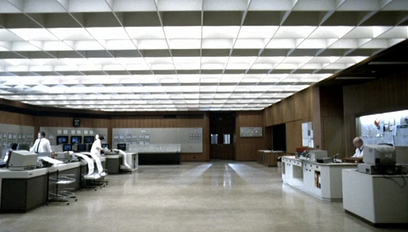The Seventh Continent (1989) movie still: wide — A spacious, sterile control room features wood-paneled walls and a large grid light ceiling.…