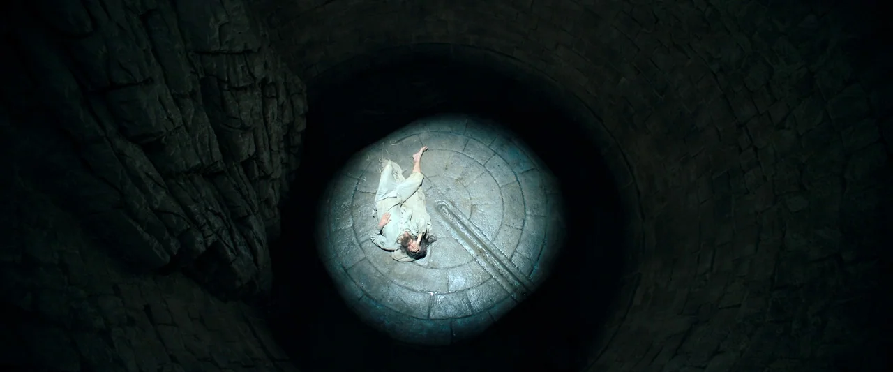 The Count of Monte-Cristo (2024) movie still: wide — A dark, circular stone well extends deep into the shadows below. A lone person lies curled on…