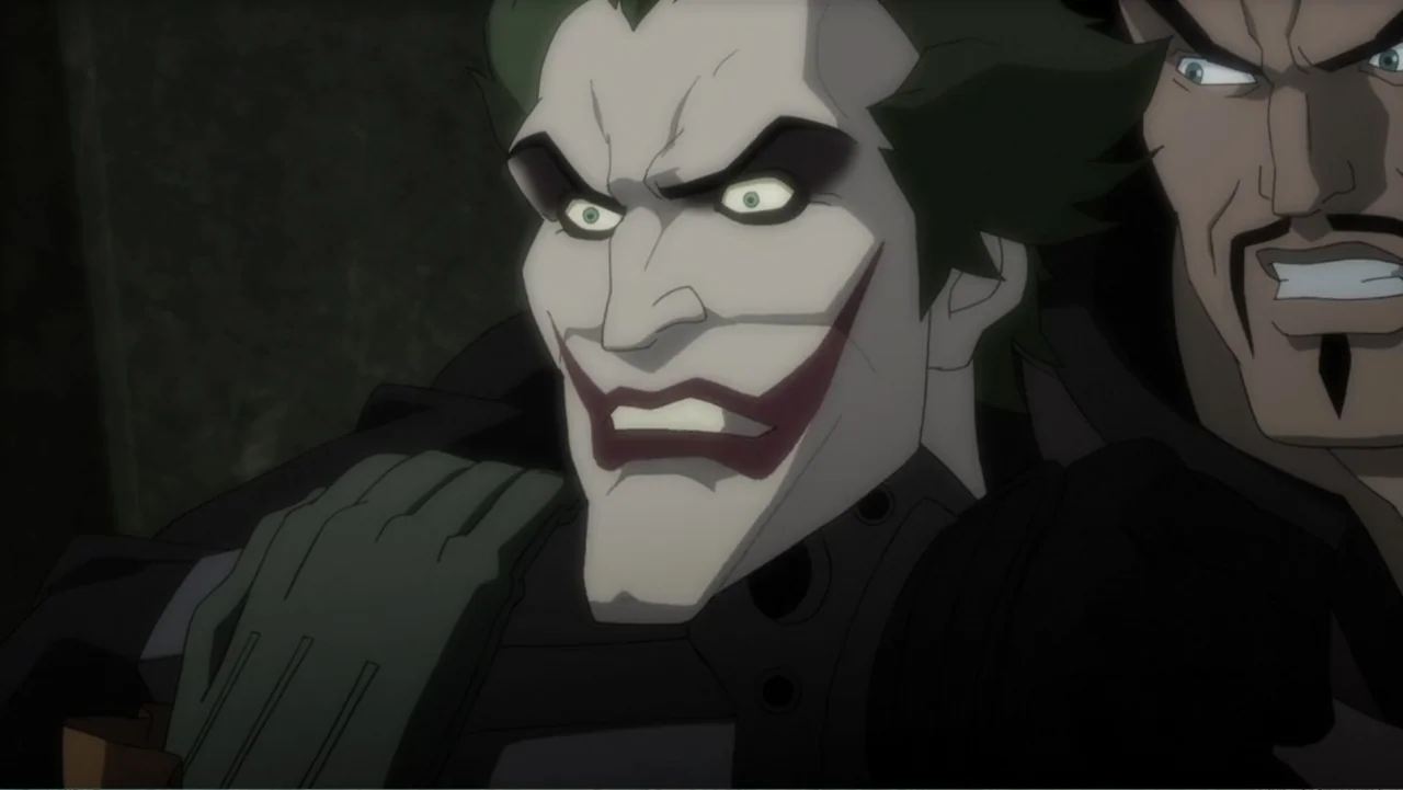 Batman: Assault on Arkham (2014) movie still: closeup — A dark indoor space with shadowed walls and industrial texture behind two men. The Joker…
