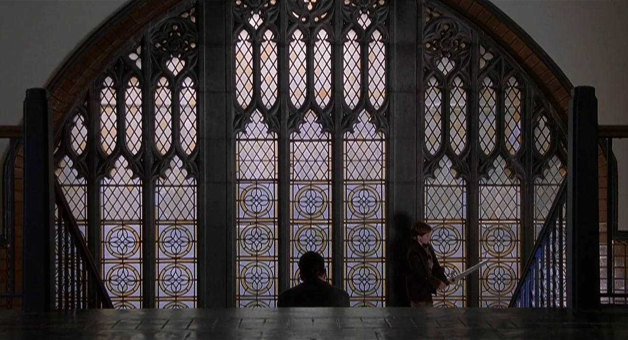 The Sixth Sense (1999) movie still: wide — A dark stairwell landing features a massive arched window with intricate leaded glass detailing. An adult…