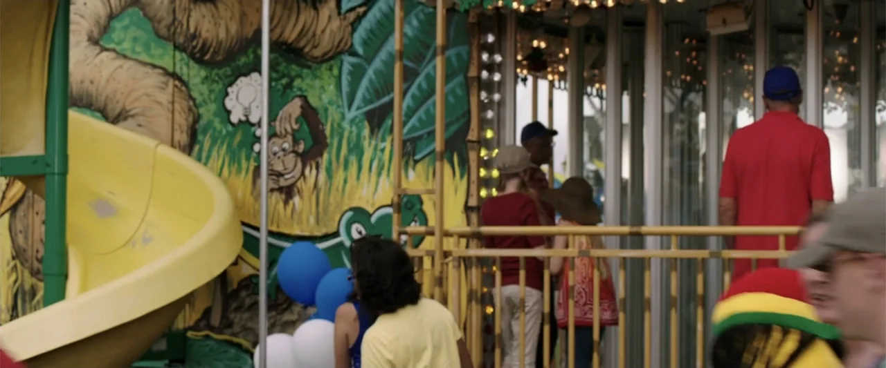 We're the Millers (2013) movie still: medium — A painted jungle-themed mural with a yellow slide sits next to a glass carousel. Several people in…