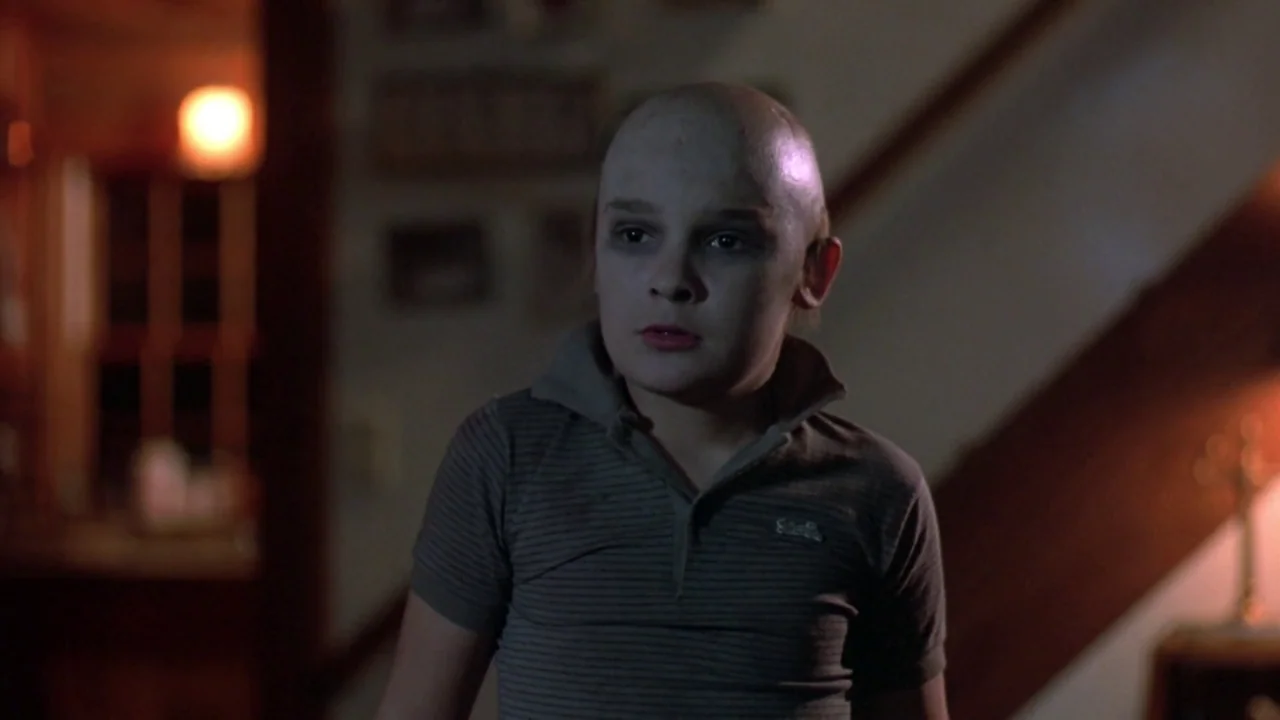Friday the 13th: The Final Chapter (1984) movie still: medium — A dimly lit indoor hallway with walls displaying small framed photographs. A bald…