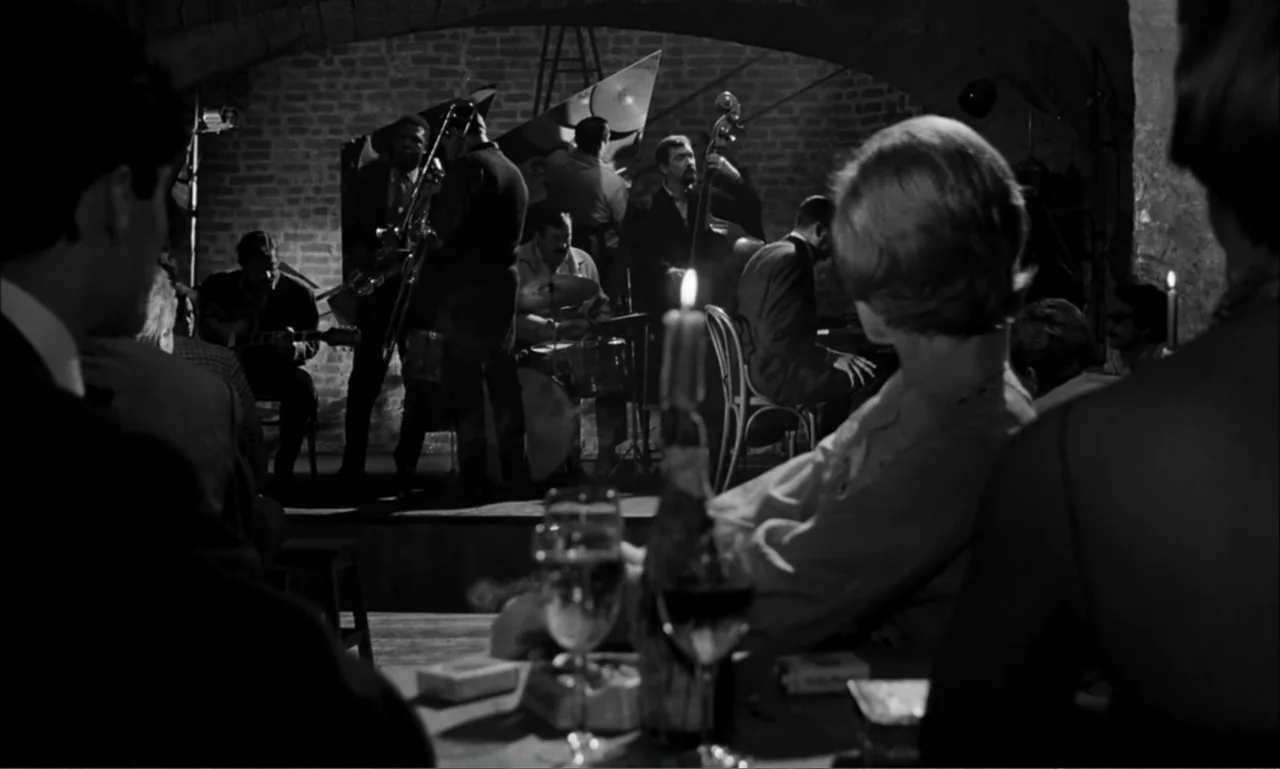 Paris Blues (1961) movie still: medium — A dimly lit jazz club features a brick wall background and arched ceiling. Patrons sit at tables in the…