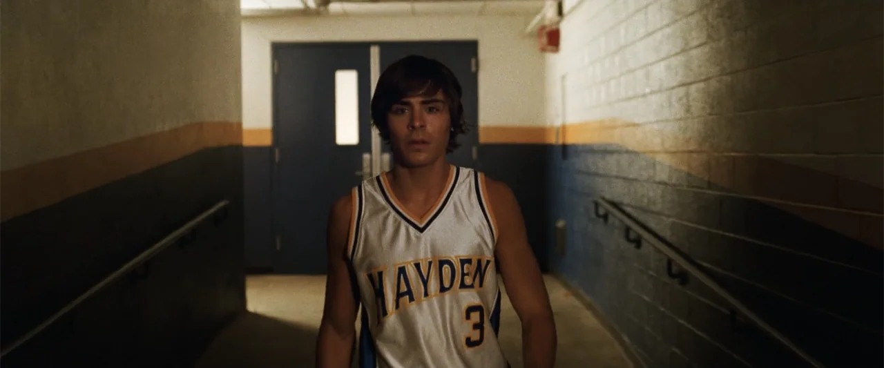 17 Again (2009) movie still: medium — A school hallway has blue and gold painted walls with metal handrails on both sides. A young male basketball…