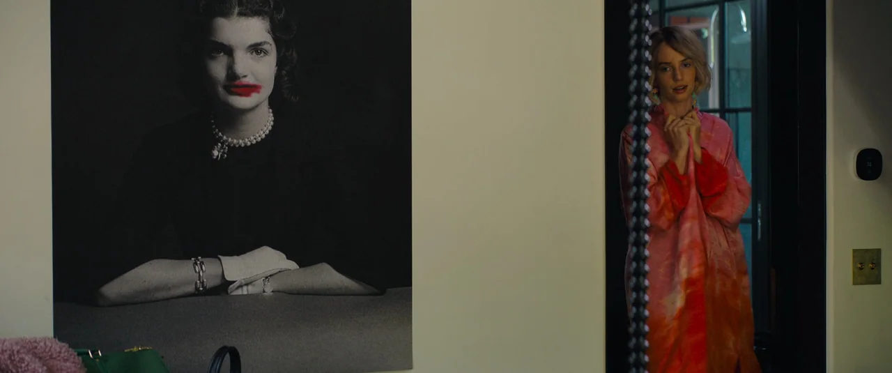 Do Revenge (2022) movie still: medium — An interior hallway features a wall-mounted black-and-white portrait of a woman with red lipstick. A young…