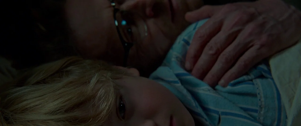 Siberia (2019) movie still: closeup — Two individuals are lying closely together in a darkened room at night. A large adult hand rests gently on the…