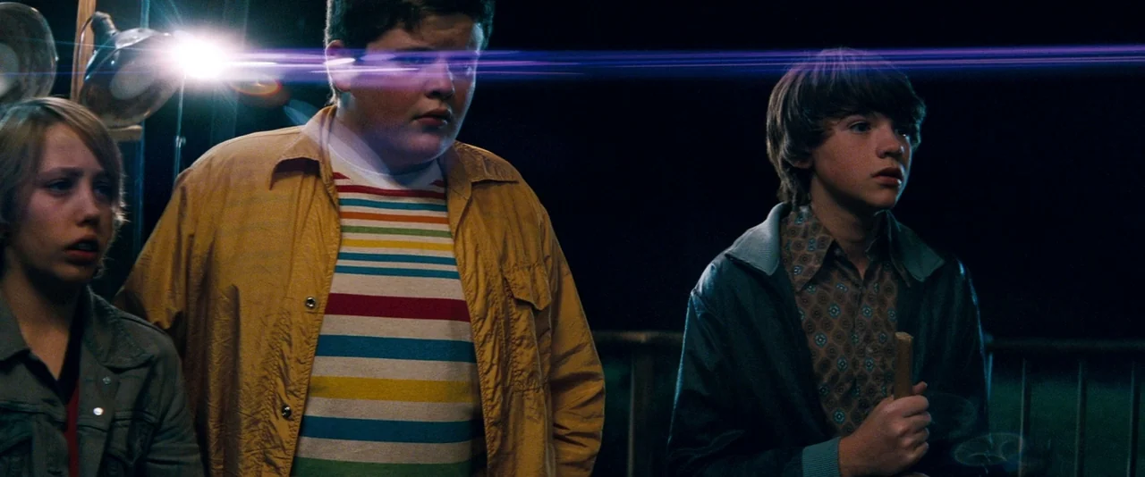 Super 8 (2011) movie still: medium — Three teenage boys stand on a deck at night under dark sky conditions. The boys look forward with wide eyes as…
