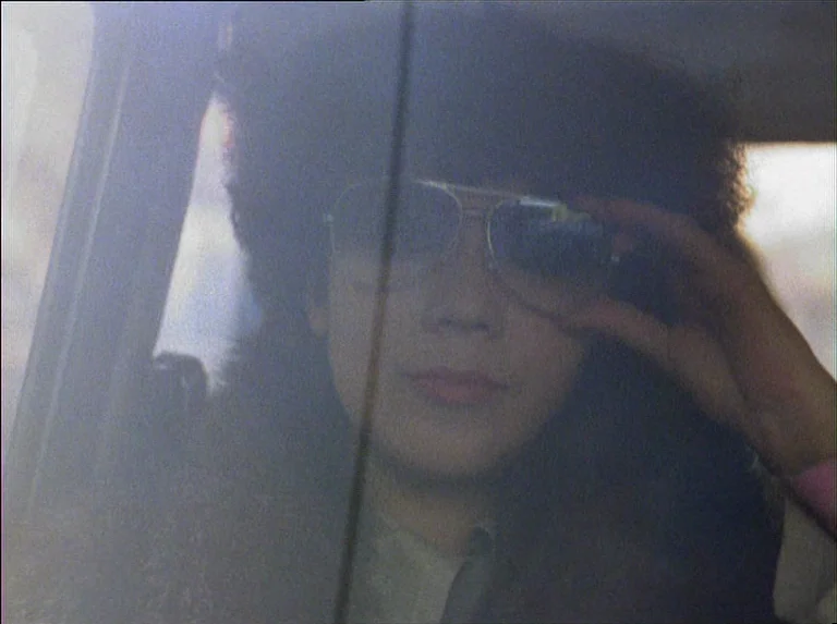 Satan’s Brew (1976) movie still: closeup — The interior of a vehicle seen through a window reflecting the outside light. A person with voluminous…