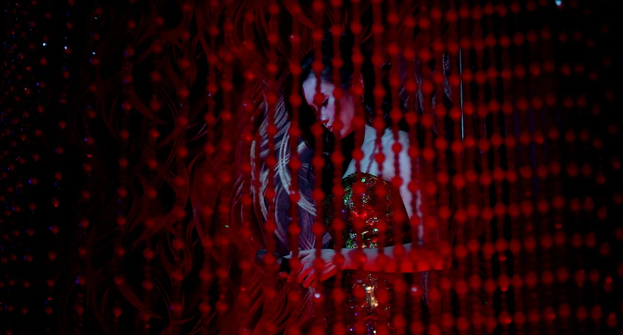 Only God Forgives (2013) movie still: medium — A dark space defined by heavy red beaded curtains obscuring the background. A woman in a sparkling…